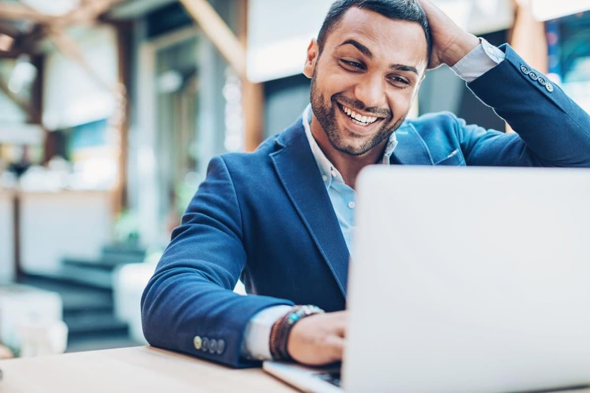Hombre de negocios sonríe frente a su laptop al ver los resultados de su estrategia DCA.