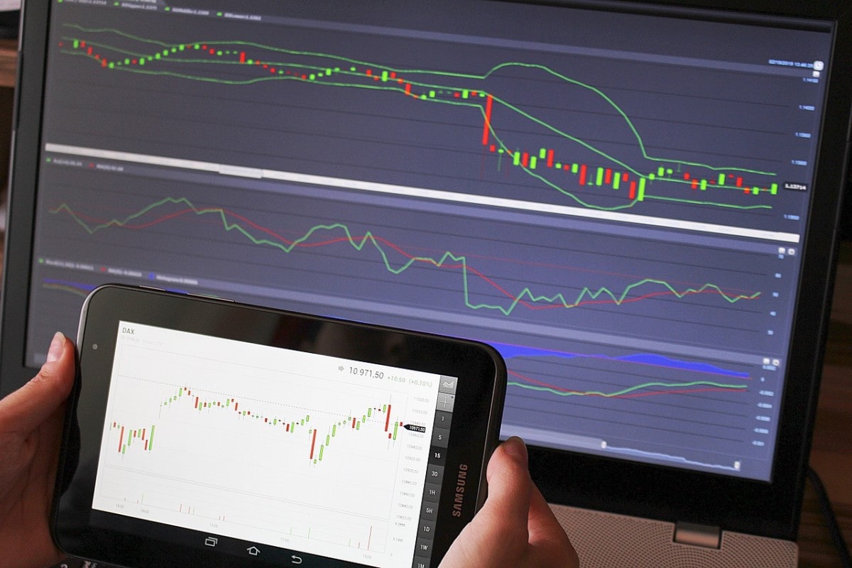 Celular y computadora con gráficos ilustrativos sobre el Dow Jones.