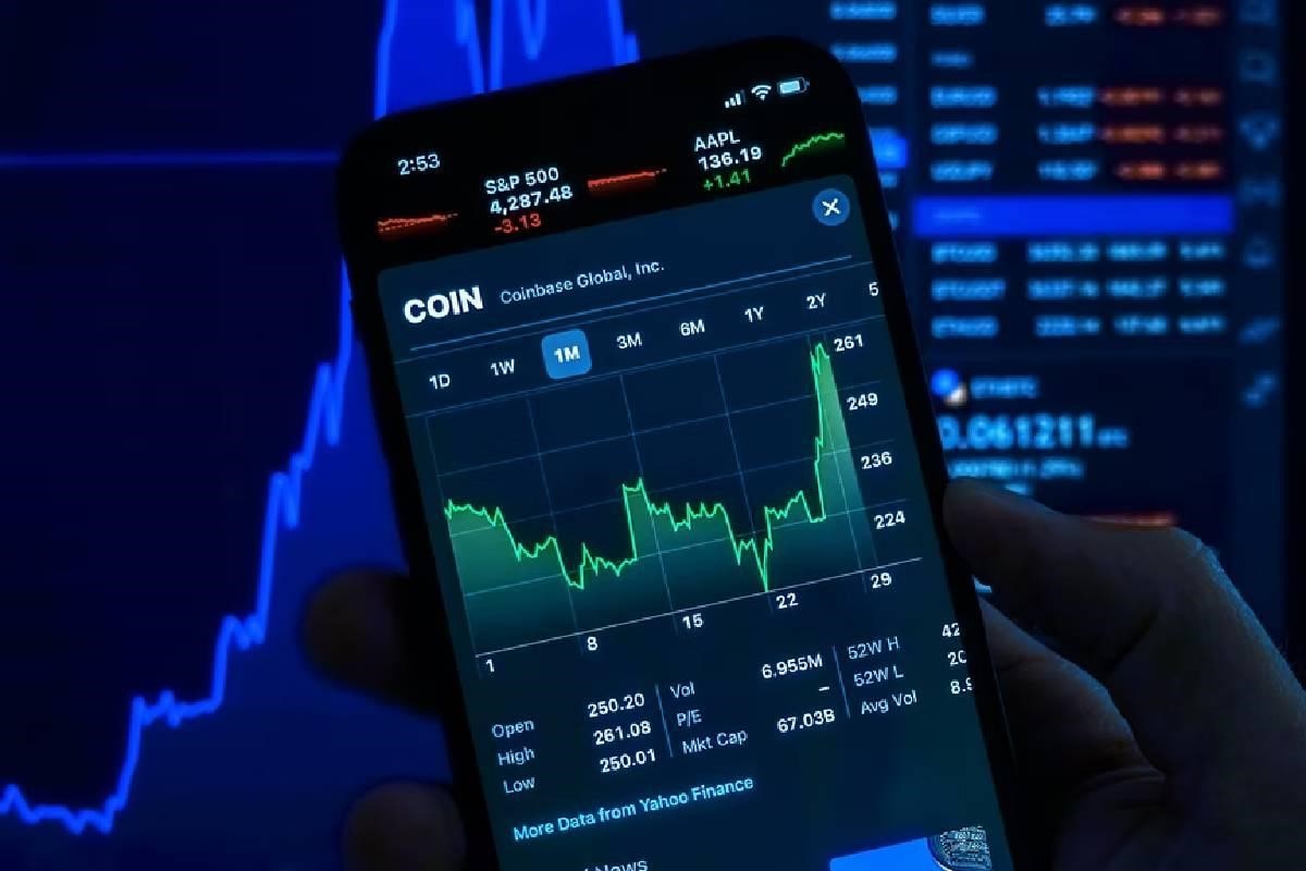 Una persona sostiene un celular y observa en su pantalla gráficos financieros.