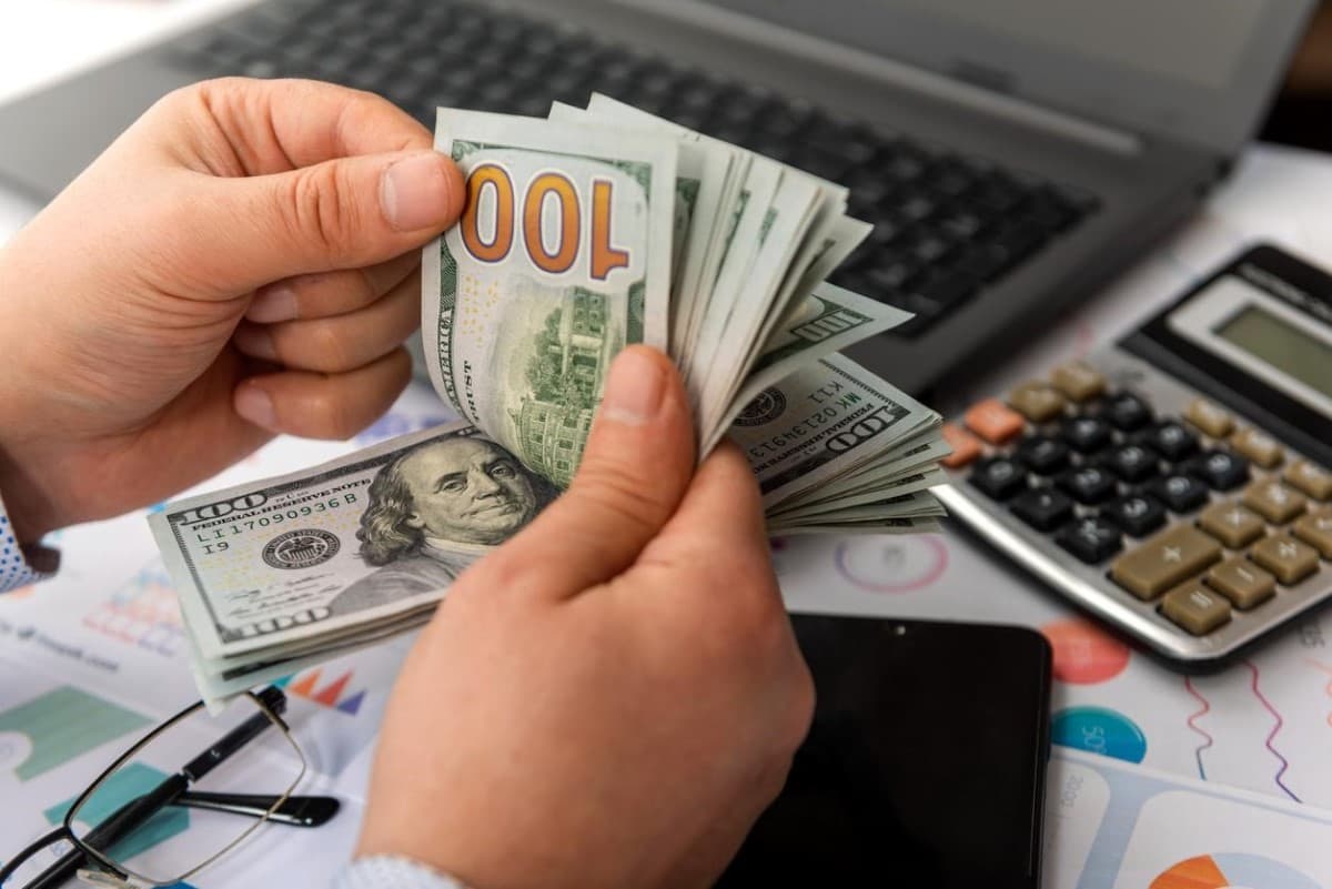 Persona cuenta billetes de 100 USD. Si te preguntas en qué invertir en Argentina, una alternativa popular es el dólar.
