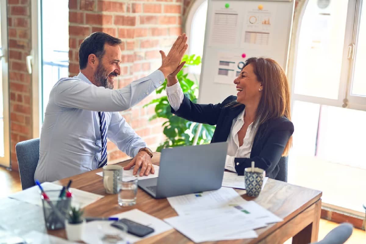 Una mujer y un hombre chocando las palmas tras ver los resultados del sistema de trading para Forex elegido.