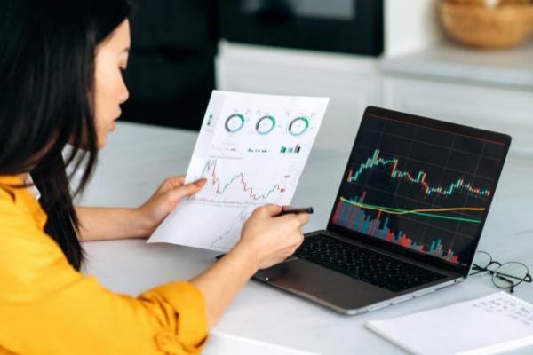 Trader revisa en una hoja y en su computadora gráficos de ETFS más rentables.